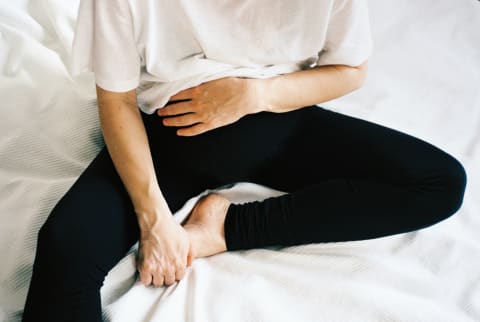 Young pregnant woman sitting on the white bed, holding her stomach and toes.